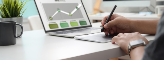 Cropped shot of graphic designer working on infographic project with drawing tablet and laptop