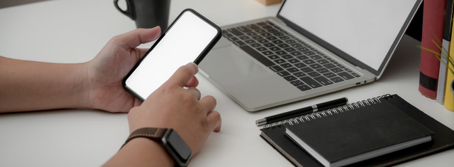 Cropped shot of businessman using blank screen smartphone while sitting at simple worktable