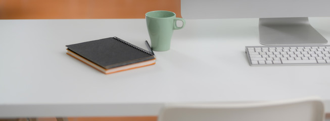 Close up view of office desk with computer device, mug and notebooks on white desk