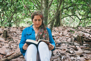 Middle-aged woman reading a book in the middle of the forest.