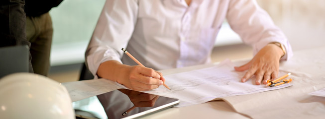 Obraz premium Cropped shot of engineer man hand drawing on blueprint and looking information on digital tablet