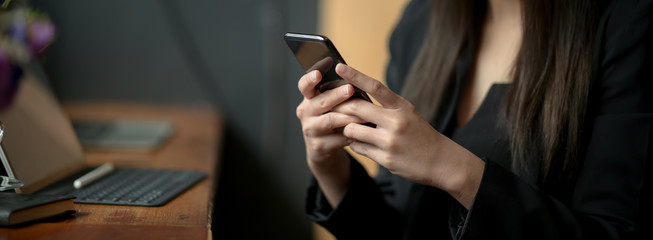 Cropped shot of female freelancer typing text message on smartphone to contact her customer