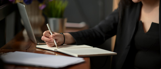 Close up view of businesswoman taking note on notebook on wooden worktable