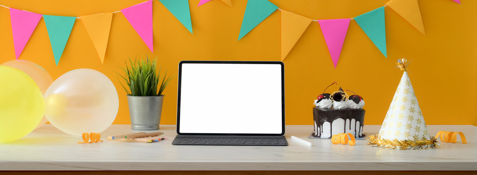 Online birthday party concept with blank screen tablet, cake and decorations