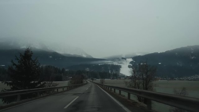 Driving on a gloomy dark road near mountains partially covered in snow