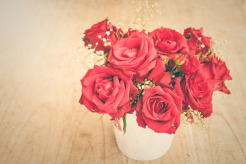 Red roses in a vase on a wooden floor
