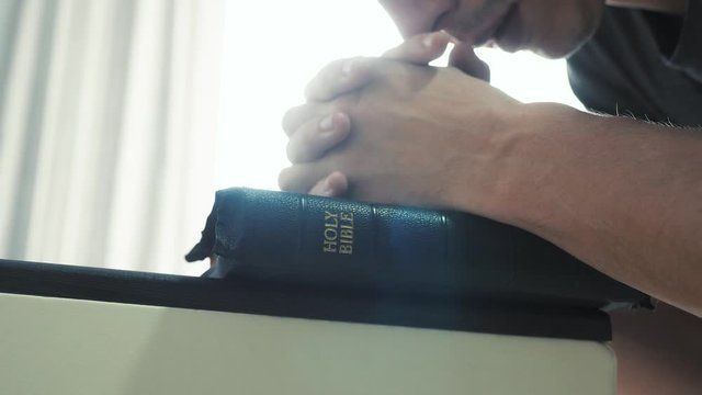 man praying indoors at bedtime on bible. religion concept evening prayer human brunette hands bible praying by bed lifestyle