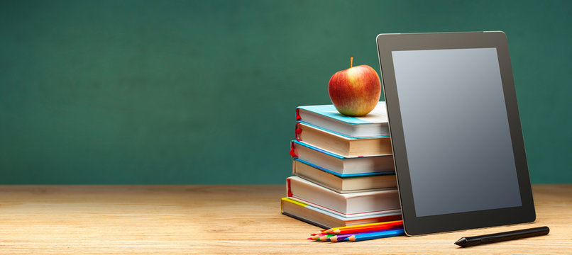 Online education. Books and tablet on the desktop on blackboard background. Copy space for text.
