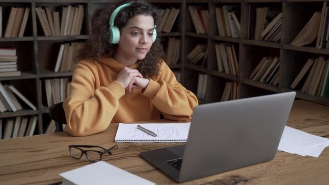 Hispanic teen girl, latin young woman school college student wear headphones learn watching online webinar webcast class looking at laptop elearning distance course or video calling teacher by webcam.