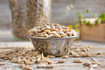 A view of a bowl filled with sunflower seed kernels, overflowing onto a rustic wood table, in a...