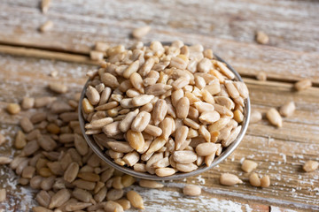A closeup view of a bowl filled with sunflower seed kernels, on a wooden table surface.
