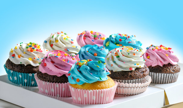 Tasty Cupcakes packaging in delivery box, various cupcakes with pink white and blue cream and colorful sprinkles on blue background