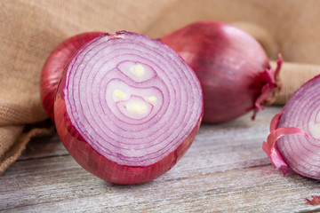 A view of several red onions, featuring one in the center that is cut open, showing the inside skin and layer texture, in a still life setting.