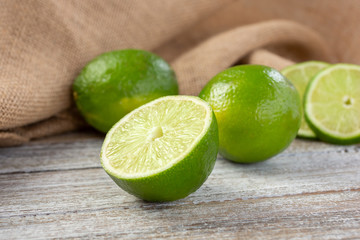 A view of several green limes, featuring on in the center that is cut open showing the segment texture, in a still life setting.