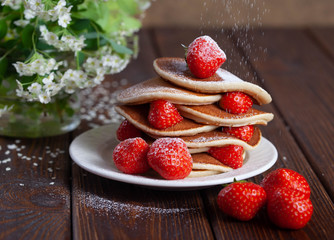 Delicious, just baked pancakes with strawberries sprinkled with powdered sugar