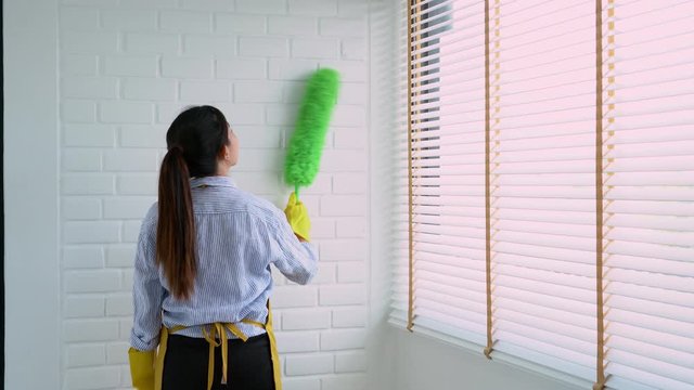 4k video of Housekeeper Young female spring cleaning house interior holding a duster for wiping dust dusting furniture at home