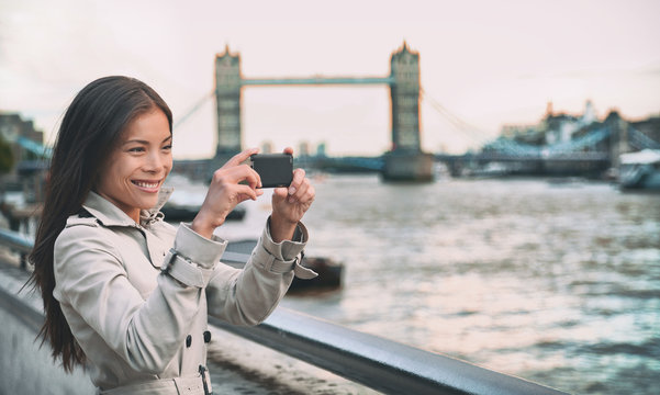 London woman tourist taking photo of Tower Bridge. London woman taking photos with mobile smart phone camera. Girl enjoying view over the River Thames, London, England, Great Britain. UK tourism.