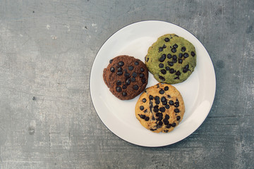 top view of various chocolate cookies on white plate on grey cement surface