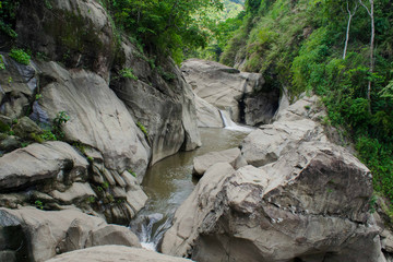 Small waterfall dropping to a stream at the center of huge rock formations. Rock formations caused by water flowing streams of water