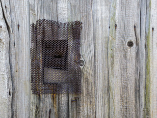 small window with perforated rusty metal grate on gray weathered wooden wall