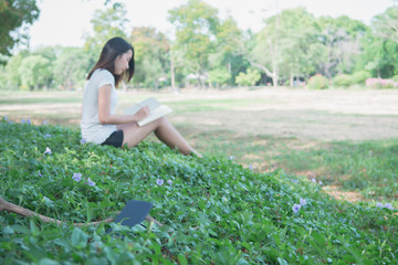 Naklejka na ściany i meble Digital detox concept. Lonely smartphone on grass because Asian beautiful woman reading a book for relaxing activity without digital technology in the park on natural light freshness morning