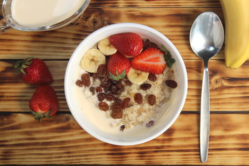 Oatmeal with raisins, strawberries, banana and yogurt on a wooden background