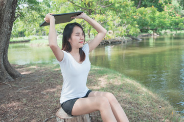 Digital detox concept. Asian beautiful woman throwing laptop for relaxing activity without digital technology in the park on natural light freshness morning