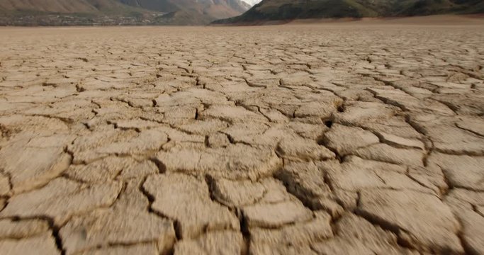 Dynamic shot of cracked soil ground of dried lake or river in mountains. Land destroyed by erosion and global warming - ecological issues concept 4k footage