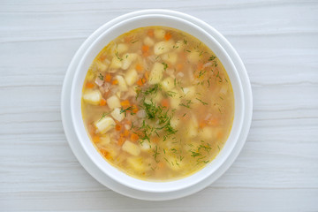 Fresh fish soup with carrots, potatoes and onions in a white plate, close up. Tasty dinner consists of a fish soup with tuna