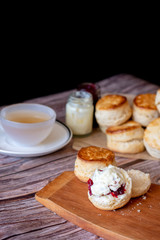 Close up group of fresh yummy tasty delicious Traditional British Scones and a cup of tea on wooden table black background.