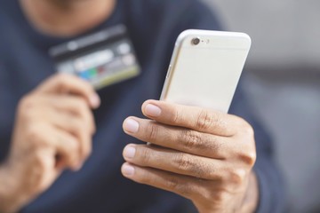 young male hands holding credit card and using phone sit order products on sofa using at home and search information Online shopping purchase Sell or Payment. 
