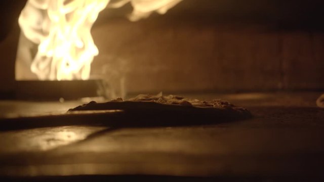 Handheld shot of pizza baking in oven and taken with shovel. Close up