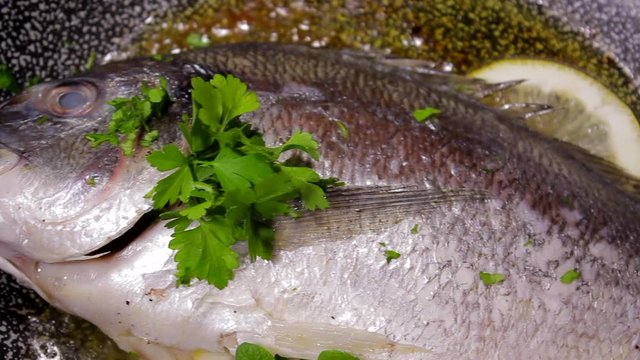 Pouring parsley on bream fish while cooking in a pan. Lemon and oil. Restaurant, home kitchen. Soft panning movement.