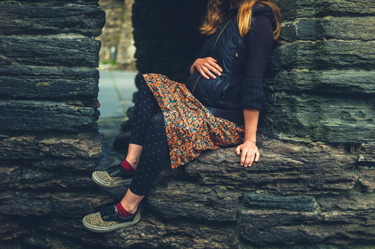 Young pregnant woman sitting on wall of old fortress