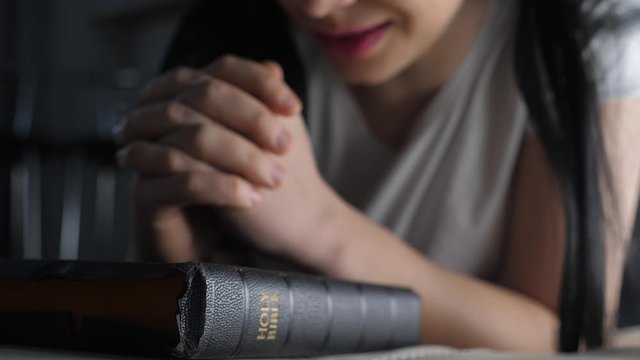 girl praying indoors at bedtime on bible. religion concept evening prayer woman brunette lifestyle hands on bible praying by bed