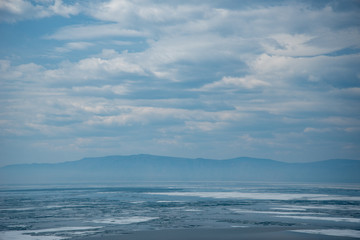 Obraz premium Natural background. Change of seasons.Baikal Lake in May morning.Spring landscape.The view from the rocks in the foreground of a snow-white fragments of ice floes. Northern nature 