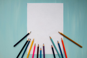 Colored pencils at the bottom of the image and a white sheet on a blue background. Flat layer, copy space, text space. The view from the top.