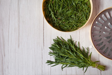 Fresh spicy spring leaves of green tarragon are placed on a dehydrator grid on a light wooden...