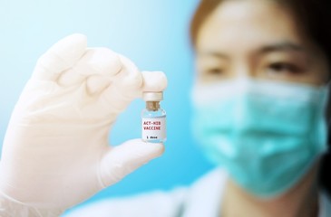 A female Asian physician with surgical mask and white rubber gloves at a clinic, holding a glass bottle of 1 dose HiB vaccine with white background and red letters.