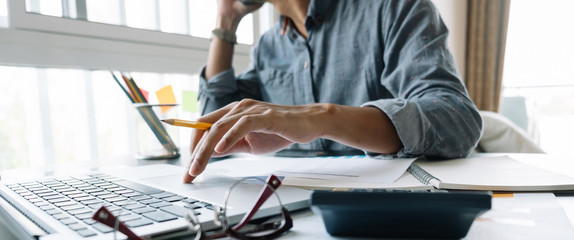 Young accountant hand holding smartphone to call marketing consultants and using laptop computer to...