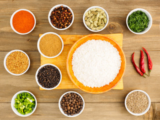 Raw white round grain rice in a bamboo bowl and spice set: red chili pepper, masala, black pepper, cumin, fenugreek, cloves, green onion, fennel