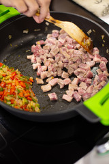 Cooking pork dices meat with vegetables on a black pan on a domestic kitchen