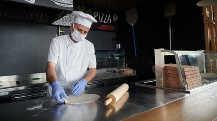 chef  with protective coronavirus face mask preparing pizza