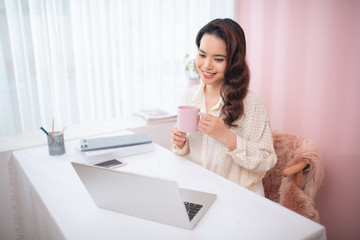 Attractive young Asian woman using laptop while drinking tea/coffee.