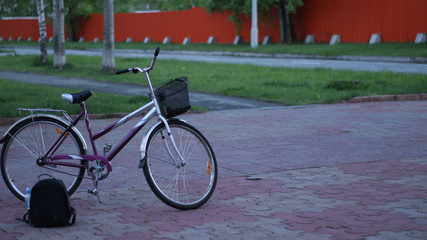 a walking bike and a black backpack are located on a deserted street amid paths and a fence in the distance