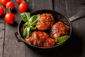 Chicken thighs and basil in a black cast-iron skillet on a wooden table
