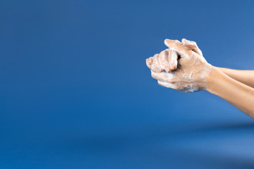 Wash your hand - coronavirus healthcare and hygiene concept. Photo of woman hands with soap foam on blue background.