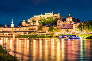 Fototapeta premium Stare miasto Salzburga odbija się w spokojnych wodach rzeki Salzach. Spektakularny nocny pejzaż Salzburga z zamkiem Hohensalzburg w tle. Austria, Europa. Podróżowanie koncepcja tło.