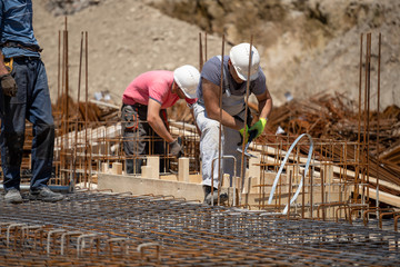 Male workers working on the retaining wall, tying rebar and reinforcement bar at the construction...