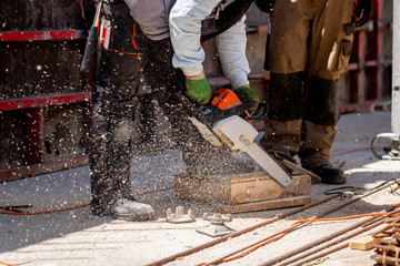 Construction worker operating with chainsaw cutting piece of wooden brick on a construction site